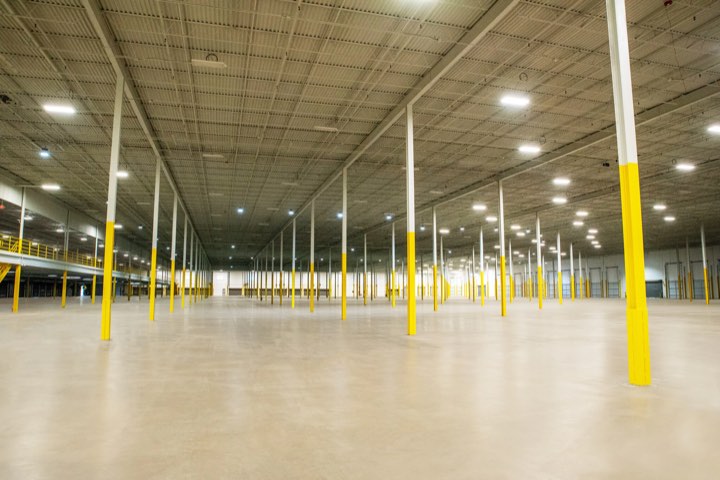 The empty warehouse floor, lit from above, with yellow painted structural columns receding into the distance.